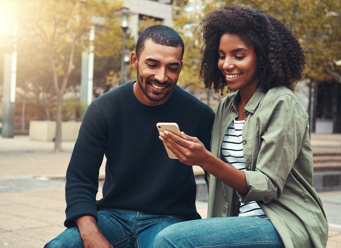 Read Our Reviews - Young Couple Looking at a Mobile Phone at the Park